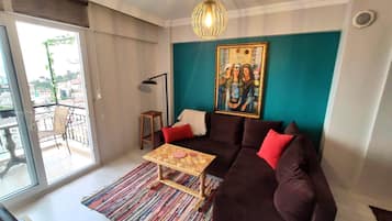 A living room with a sofa, a coffee table, a painting, and a view through a large window.