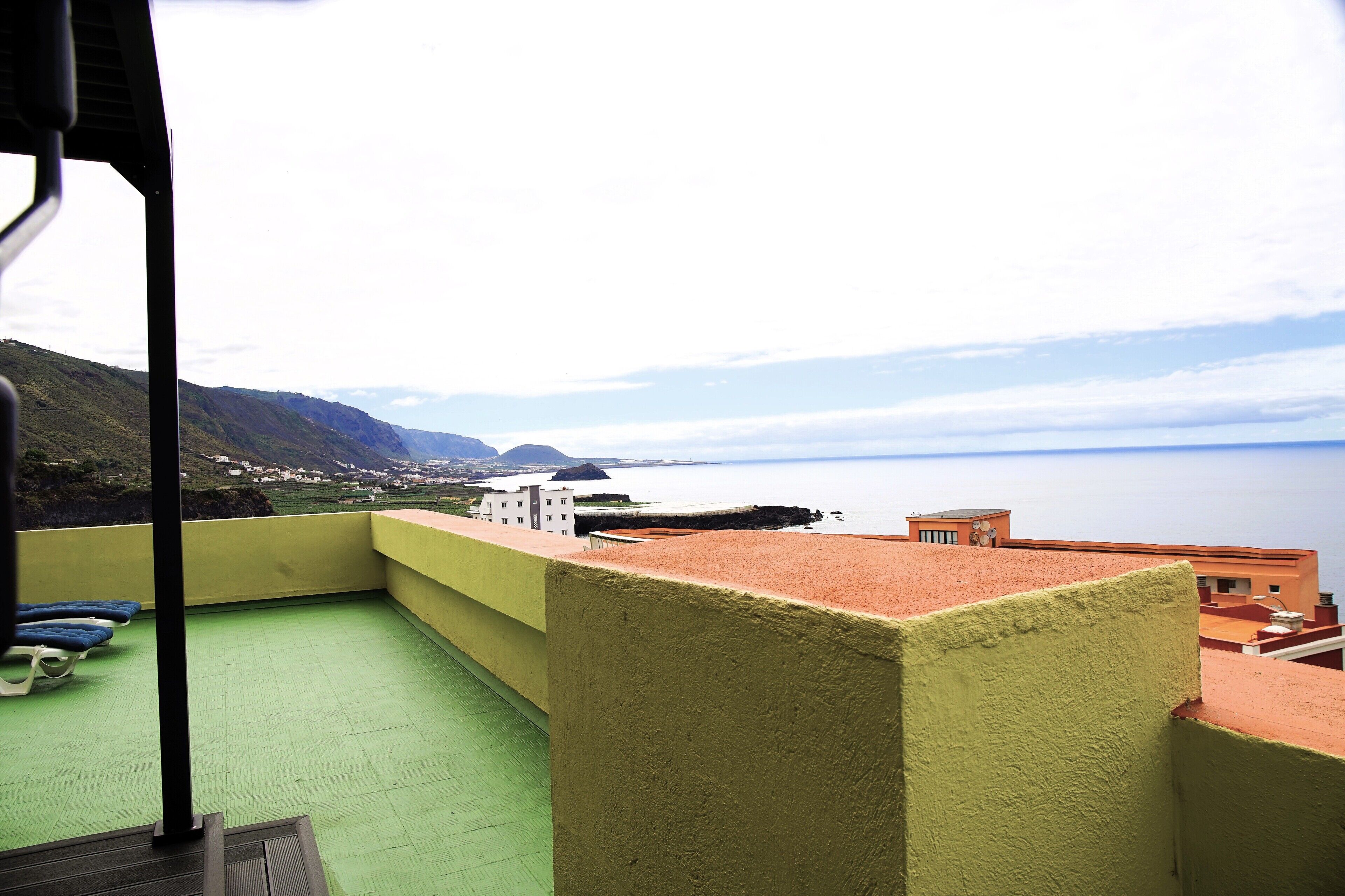 Un balcón con suelo verde, vistas a un pueblo costero y una masa de agua.
