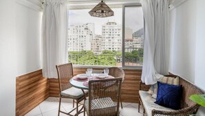 Un balcón con mobiliario de mimbre, una mesa para dos personas y vistas a edificios altos.