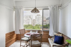 Un balcón con mobiliario de mimbre, una mesa para dos personas y vistas a edificios altos.