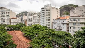 Un paisaje urbano con edificios de varios pisos, una colina destacada al fondo y un tejado rojo a la vista en primer plano.