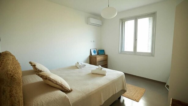 Un dormitorio con cama, mesita de noche, ventana y unidad de aire acondicionado.