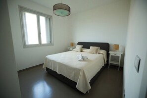 A bedroom with a bed, a window, a bedside table, and a hanging light fixture. - Villa Zabbara (Favignana)