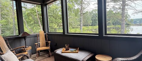 Quarto aconchegante com ventoinha no teto, janelas amplas, móveis de vime e vista para uma floresta.