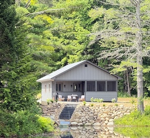 A cabin with a stone staircase leading to a deck, surrounded by dense forest.