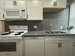 A kitchen with white cabinets, a granite countertop, a stainless steel sink, and a microwave. - 2BR Sunny Haven Near Short North (Columbus)