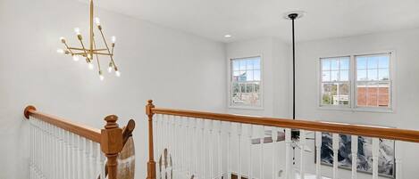 A staircase with a wooden handrail and white balusters, leading to a balcony with a view of the city.