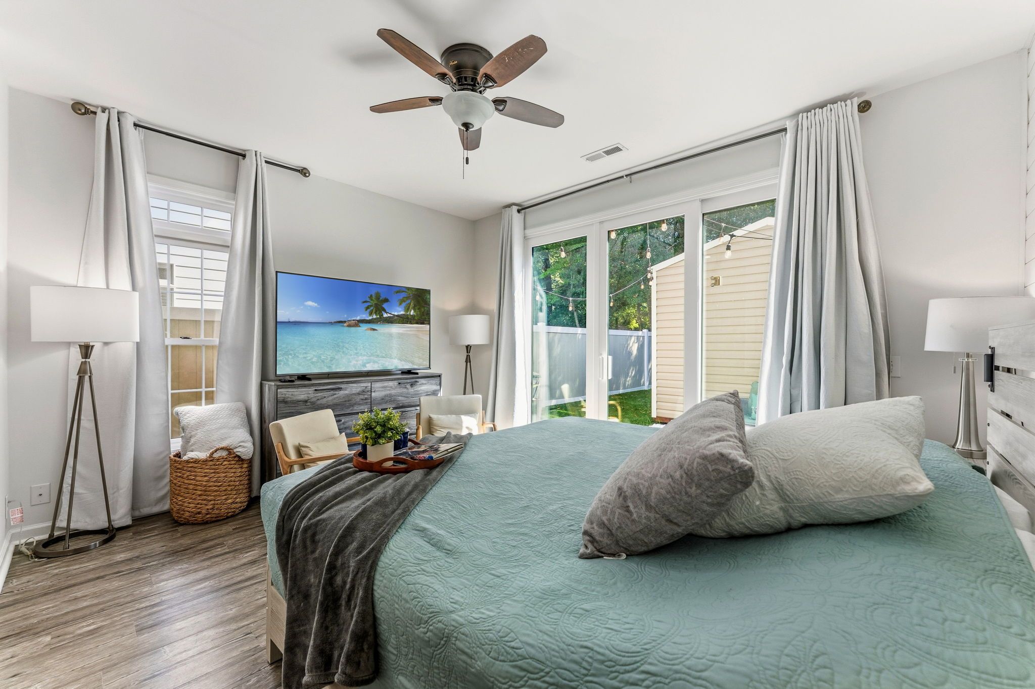 A bedroom with a bed, a ceiling fan, a TV, and a window with curtains.