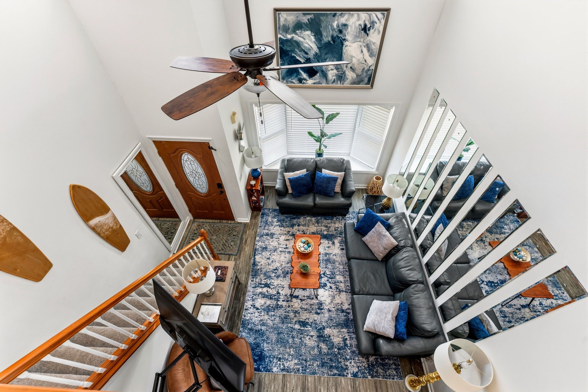 A spacious living area with a black leather sofa, a blue patterned rug, and a ceiling fan.
