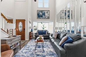 A spacious living room with a leather sofa, a coffee table, and a large abstract painting above the sofa. - Designer Family Beach House · Walk to Sand & Golf (North Myrtle beach)