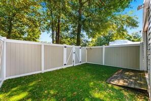 Une cour arrière clôturée avec une pelouse et une terrasse en bois.