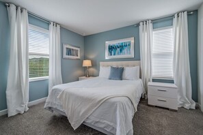 Ein Schlafzimmer mit einem Bett, Nachttischen, einer Lampe und zwei gerahmten Bildern an der Wand.