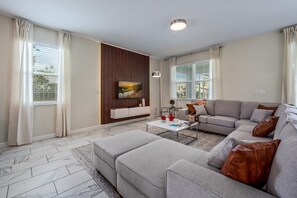 Ein modernes Wohnzimmer mit einem Ecksofa, einem an einer Holzvertäfelung montierten Flachbildfernseher, einem Couchtisch und einem gemusterten Teppich.