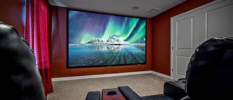 A home theater room with a large flat-screen TV displaying the Northern Lights, a red curtain, and a white door.