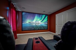Ein Heimkino mit einem großen Flachbildfernseher, der das Nordlicht zeigt, einem roten Vorhang und einer weißen Tür.