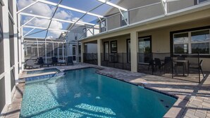 A swimming pool with a glass enclosure, lounge chairs, and a patio area with outdoor furniture. - 8-bedroom House - Championsgate With Pool (Davenport)