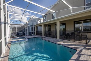 Ein Schwimmbad mit Glasveranda, Liegestühlen und einer Terrassenanlage mit Gartenmöbeln.