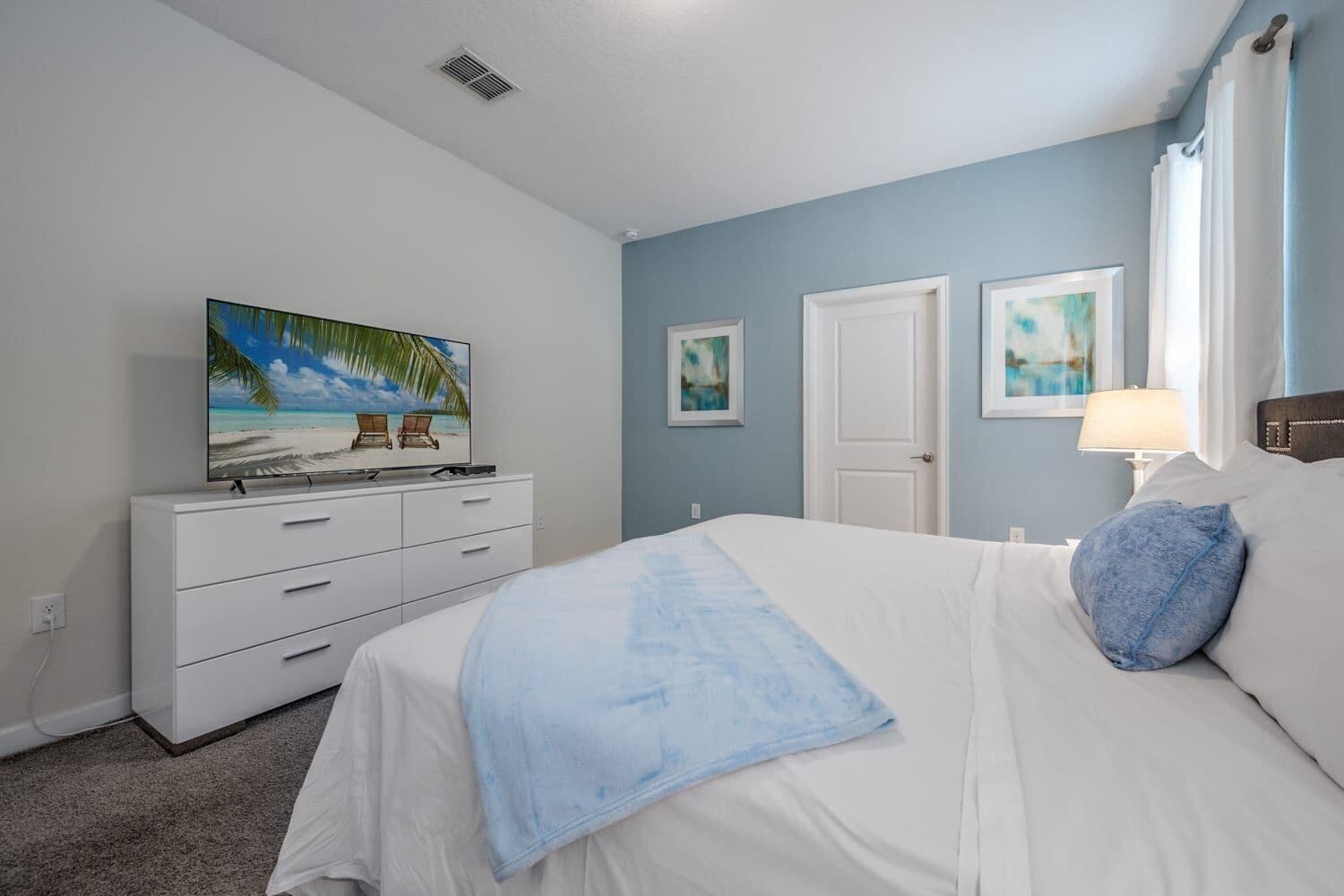 A bedroom with a bed, a dresser, a television, and two framed pictures on the wall.