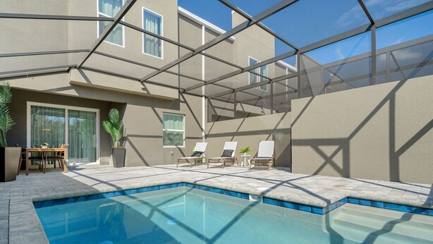 A swimming pool with a glass enclosure, lounge chairs, and a table with chairs. - Modern 5BR Home Near Disney With Private Pool (Davenport)