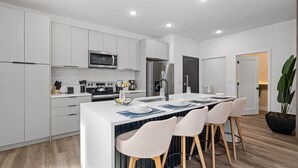 A modern kitchen with white cabinetry, a central island with bar seating, and a stainless steel refrigerator. - Modern 5BR Home Near Disney With Private Pool (Davenport)
