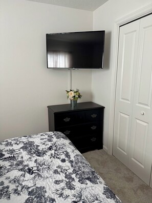 A bedroom with a bed, a dresser, a television mounted on the wall, and a door. - Cozy 2 bedroom 2 bath villa in exciting new Eastport.  Village of Edenfield. (Sumterville)