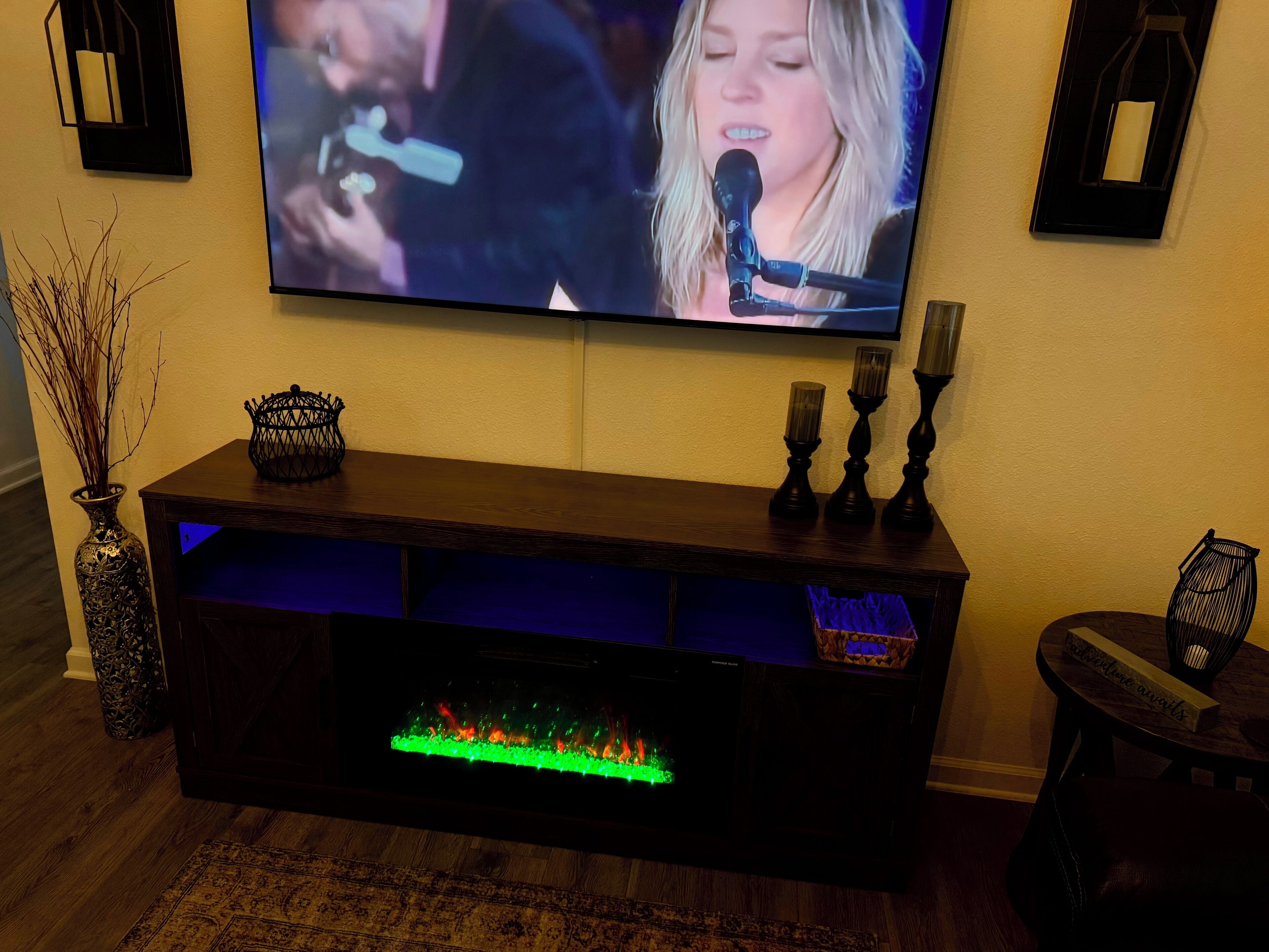 Ein an der Wand befestigter Fernseher, eine dunkelholzene Unterhaltungsanlage mit Kamin und dekorative Gegenstände auf den Regalen.