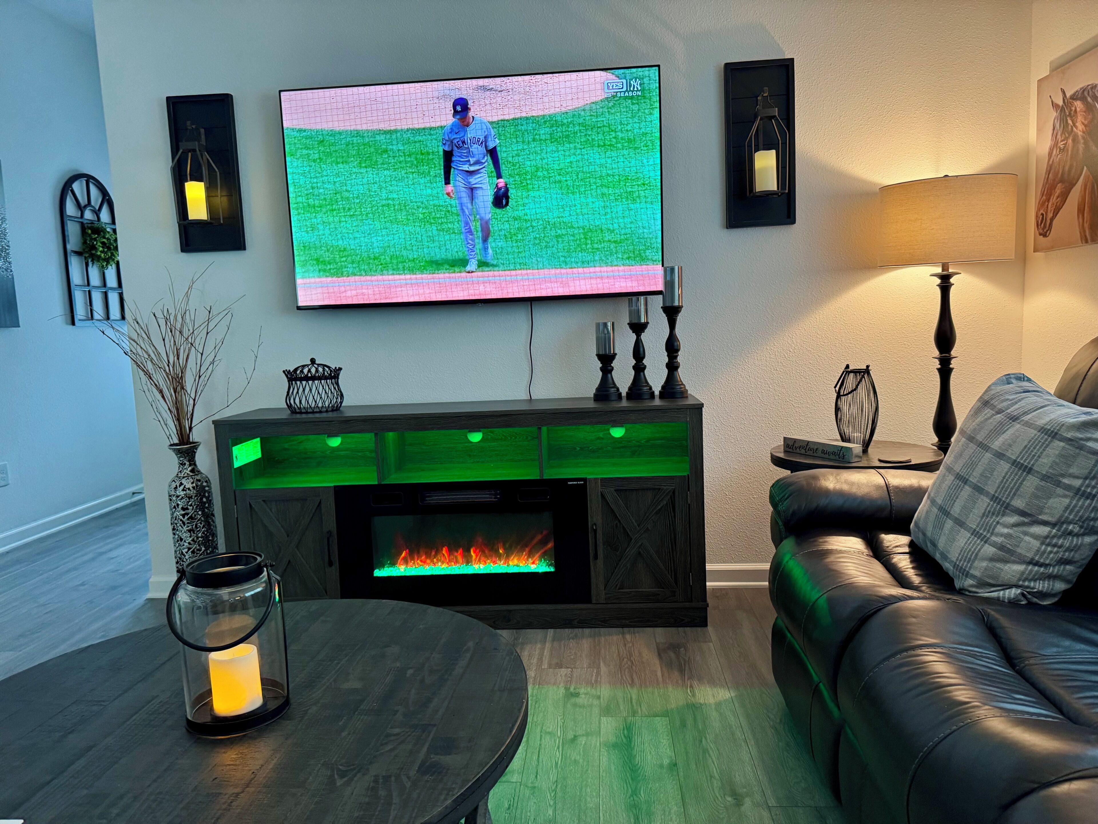 Sala de estar com televisão de tela plana na parede, lareira com base iluminada em verde, sofá de couro e mesa de centro.