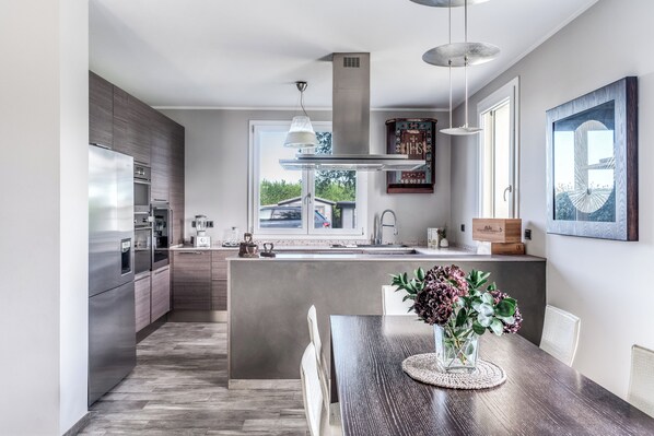 Una cocina moderna con una isla central, electrodomésticos de acero inoxidable y un comedor con un jarrón de flores.