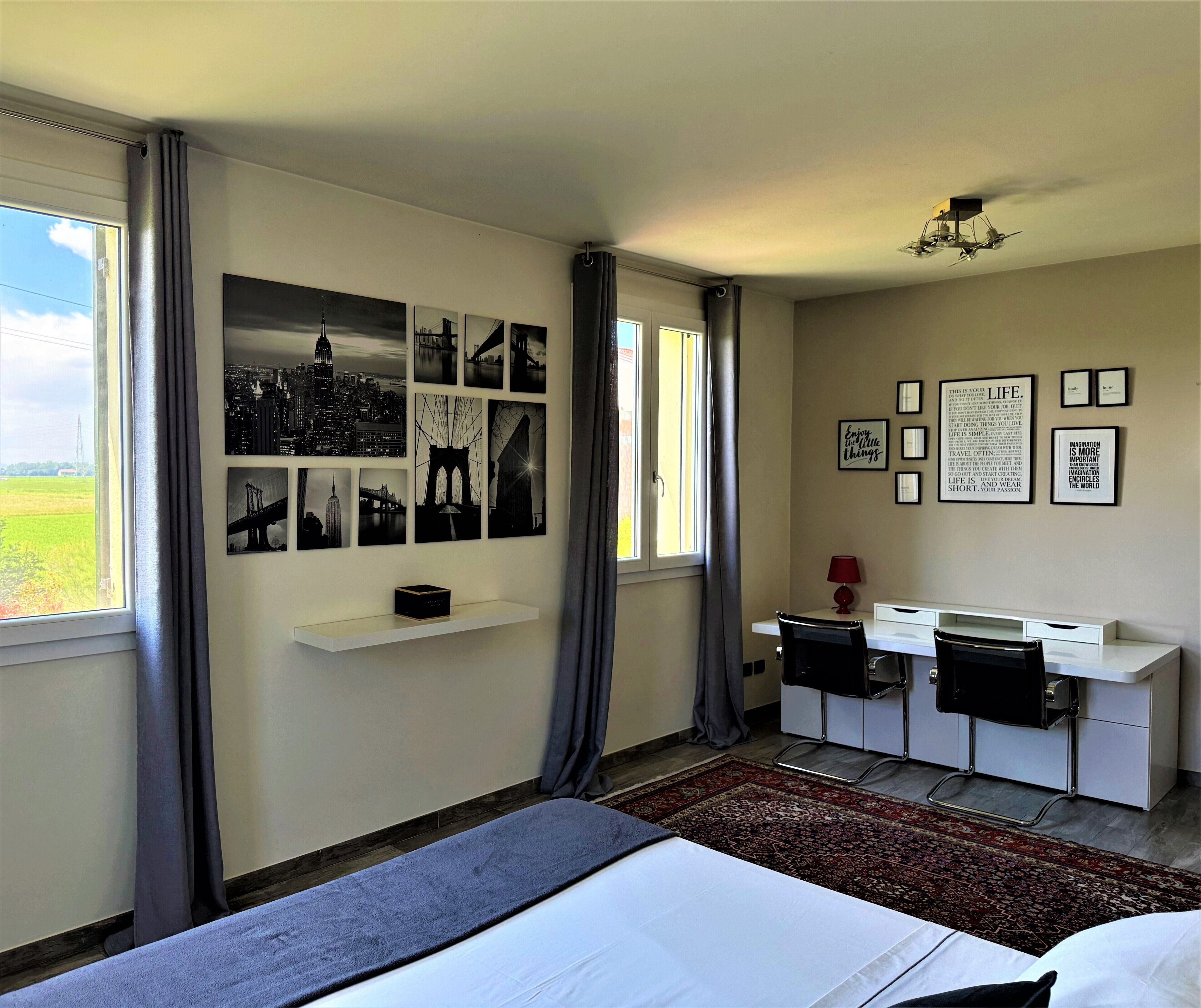 A hotel room with a bed, a desk, and a chair. There are pictures on the wall and a window with curtains.
