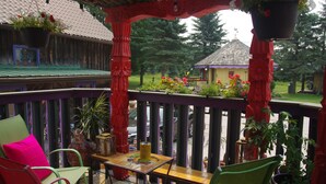 A covered outdoor seating area with chairs and tables, surrounded by potted plants and a view of a building in the background.