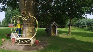 A tree with a heart-shaped structure around it, a small wooden house, and a dog in a fenced area.