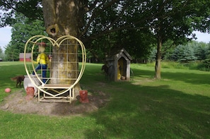 A tree with a heart-shaped structure around it, a small wooden house, and a dog in a fenced area.
