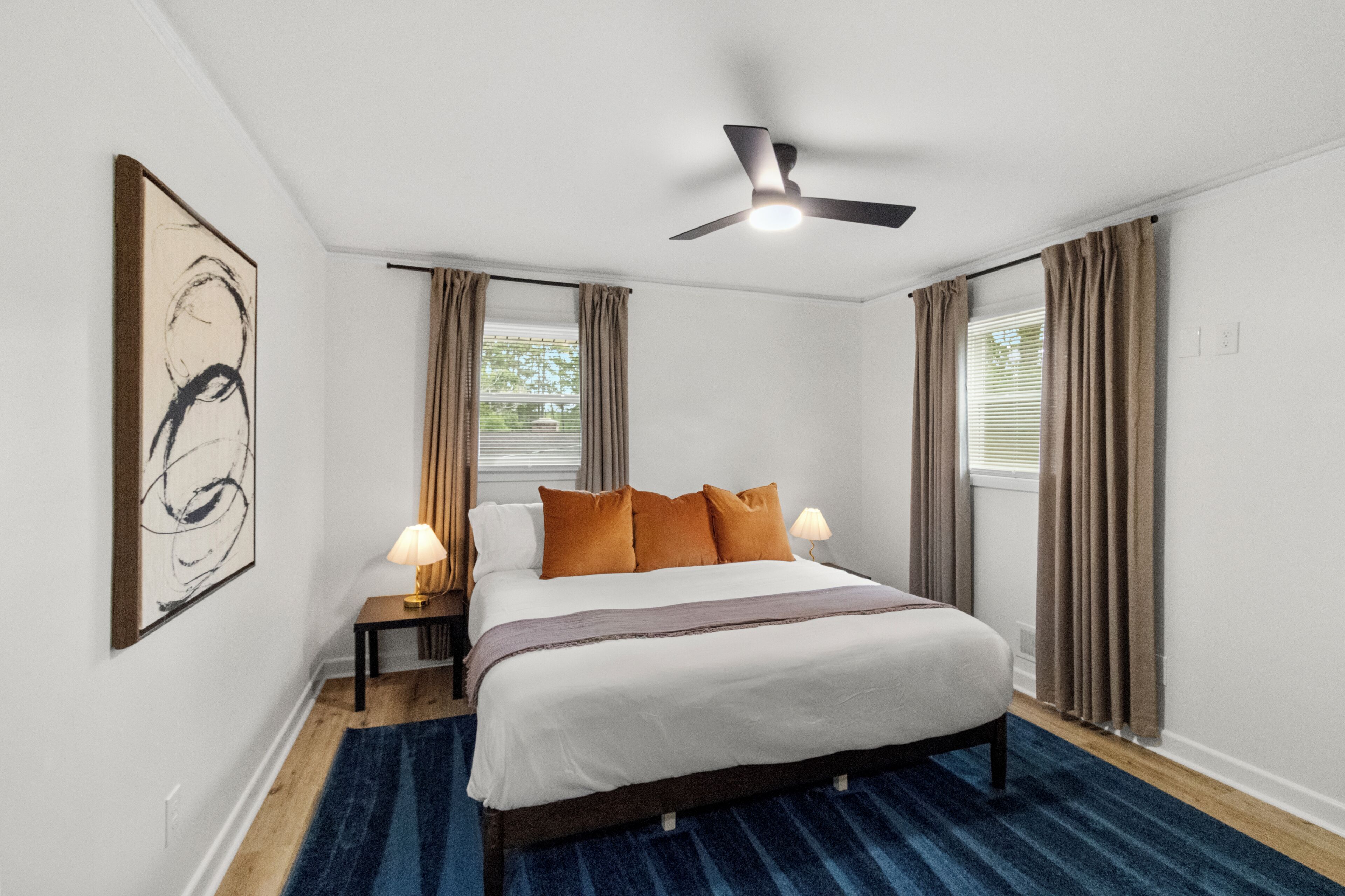 Een hotelkamer met een bed, twee bedlampen, een plafondventilator en een groot abstract schilderij aan de muur.
