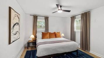 Een hotelkamer met een bed, twee bedlampen, een plafondventilator en een groot abstract schilderij aan de muur.