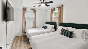 A hotel room with two beds, a ceiling fan, a TV, and a window with curtains.