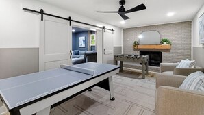 A room with a ping pong table, a foosball table, a sofa, and a fireplace.