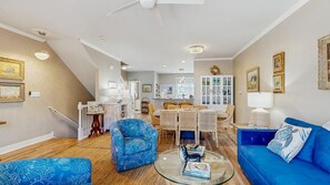 Ein geräumiges Wohnzimmer mit einem blauen Sofa, einem Glastisch und einer Essecke mit Korbmöbeln.