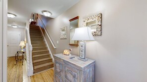 A staircase with a wooden handrail, a white door, a small table with a lamp, and a decorative mirror on the wall. - Rehoboth Crossing - 36983 Grindstone Ln (Rehoboth Beach)