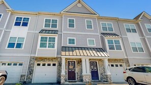 A multi-story residential building with a stone facade, multiple garage doors, and a symmetrical design. - Rehoboth Crossing - 36983 Grindstone Ln (Rehoboth Beach)