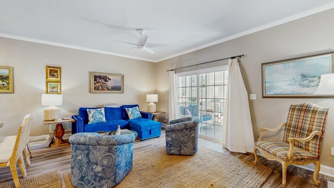 A living room with a blue sofa, patterned ottomans, a plaid armchair, and a large window with curtains.
