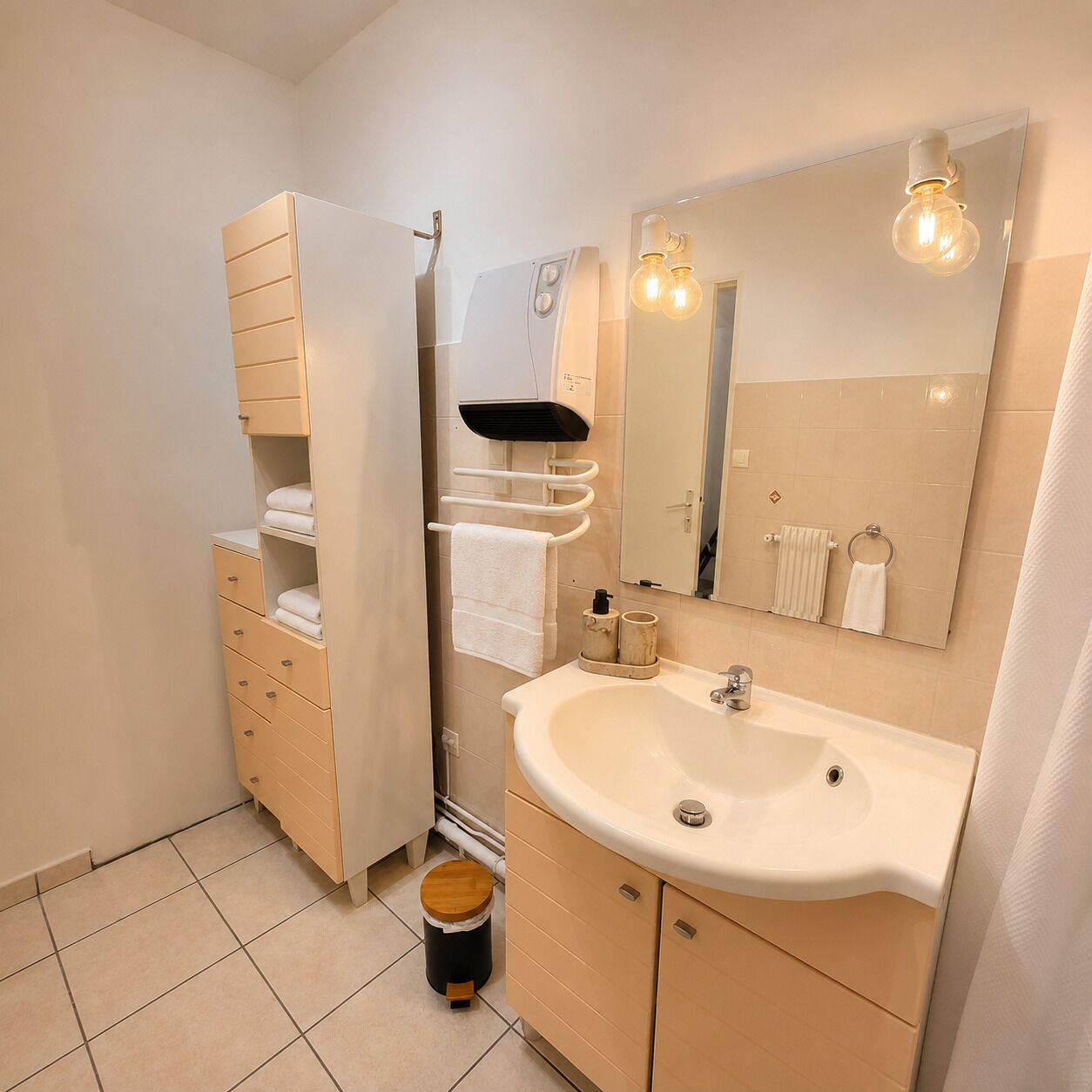 Um banheiro com pia, espelho, porta-toalhas e armário para guardar objetos.