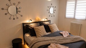 A bedroom with a bed, bedside lamps, a round mirror, and a radiator. - The Butterfly Garden (La Buisse)