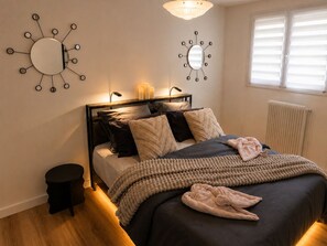 A bedroom with a bed, bedside lamps, a round mirror, and a radiator. - The Butterfly Garden (La Buisse)