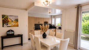A modern dining area with a white table and chairs, a black console table with a vase, and a painting on the wall. - The Butterfly Garden (La Buisse)