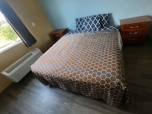 A bedroom with a bed, a nightstand, a dresser, and a window with curtains.