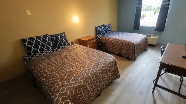 Quarto com duas camas, uma mesa de cabeceira de madeira, uma mesa e uma janela com cortinas.
