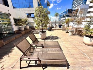 An outdoor seating area with lounge chairs and potted plants. - Santa Mônica Residen (São Paulo)