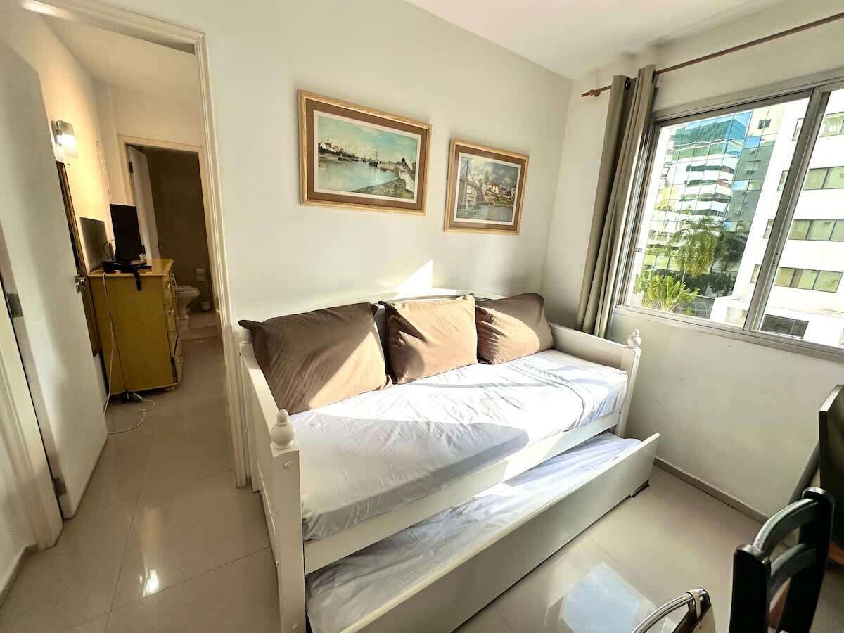 Quarto com cama, escrivaninha e janela com vista para edifícios.