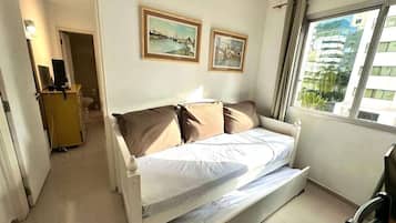 Quarto com cama, escrivaninha e janela com vista para edifícios.