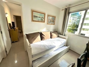 Un dormitorio con cama, escritorio y ventana con vistas a edificios.